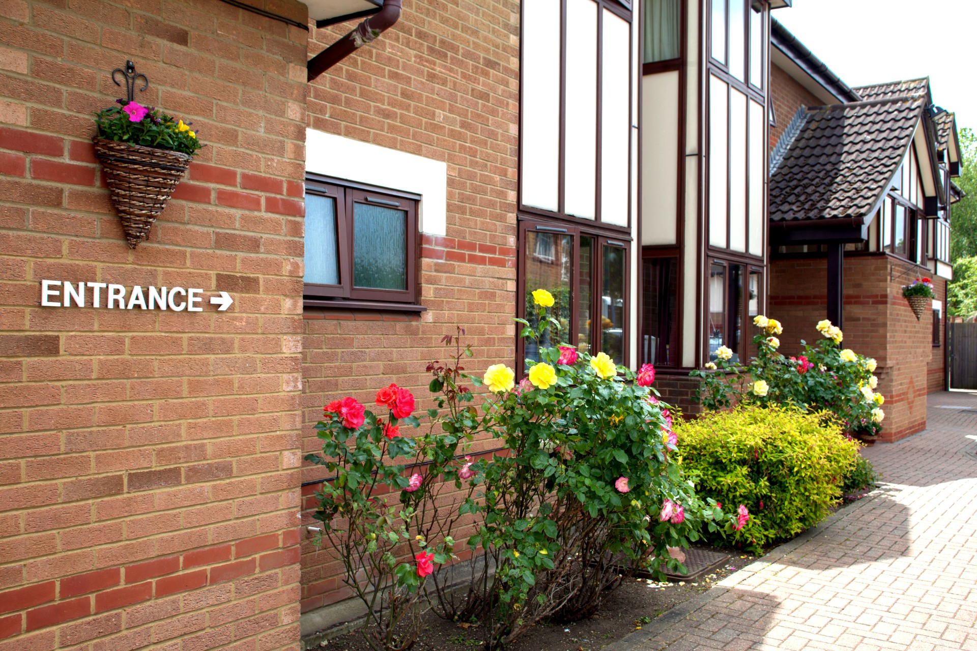 The entrance to Bletchley House, a care home in Milton Keynes, featuring colorful rose bushes and a hanging flower basket.