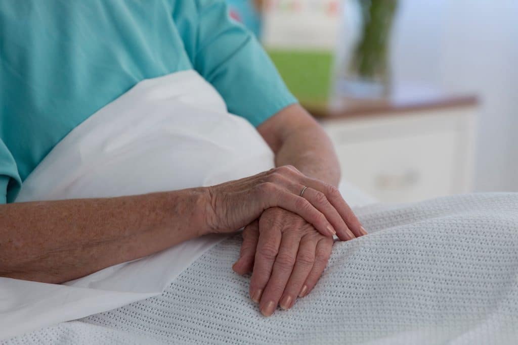 hands folded on white bed sheets