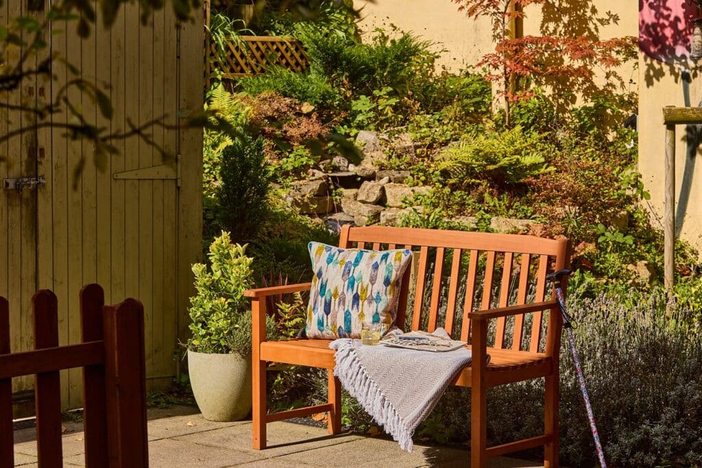 Wooden garden bench with cushion and throw