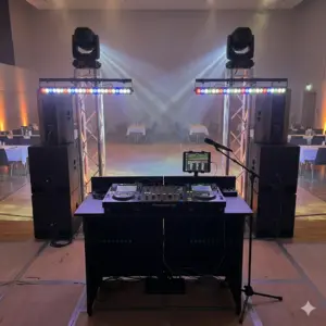 Professionelles DJ-Anlagen Großset Gemini_Generated_Image_nt8007nt8007nt80.png für Hallenpartys und Zeltfeten. Im Vordergrund steht ein schwarzes DJ-Pult mit einem Pioneer DJ-Setup (zwei Mediaplayer und Mischpult), einem Funkmikrofon auf Stativ sowie einem Tablet für die DMX-Lichtsteuerung. Flankiert wird das System von einer massiven PA-Anlage mit Doppel-Subwoofern und zwei Traversensäulen (Truss), auf denen sich LED-Bars und rotierende, lichtstarke Moving Heads im Hallenhintergrund befinden.