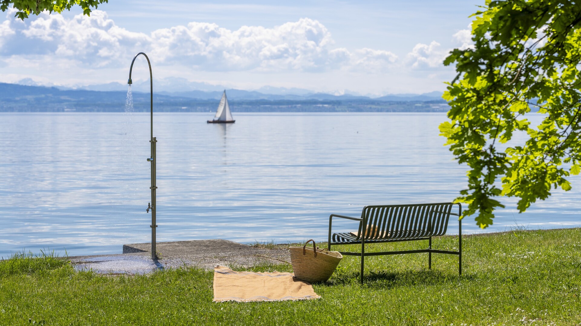 Privater Seezugang am Bodensee mit Außendusche, Sitzbank und Liegewiese am Ufer, Segelboot und Berge im Hintergrund