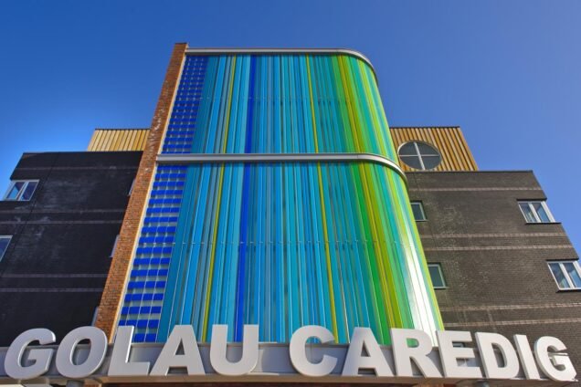 Exterior of the Golau Caredig building, featuring a curved facade with blue and green panels, and silver signage.