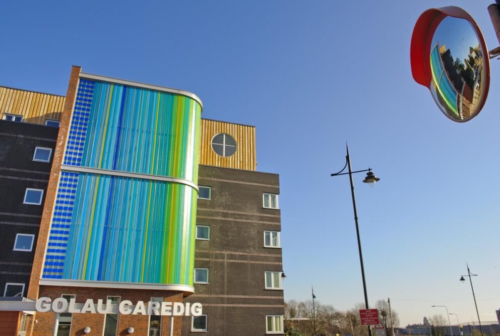 Modern building with a curved, striped facade in blue and green, wood cladding, and dark brickwork.