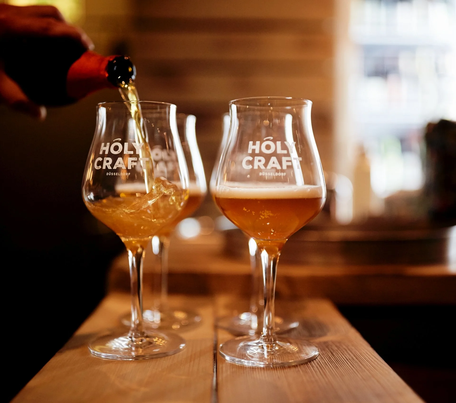 Ein Hand goss ein Bier in ein Glas am Tisch. Es gibt zwei Gläser mit 