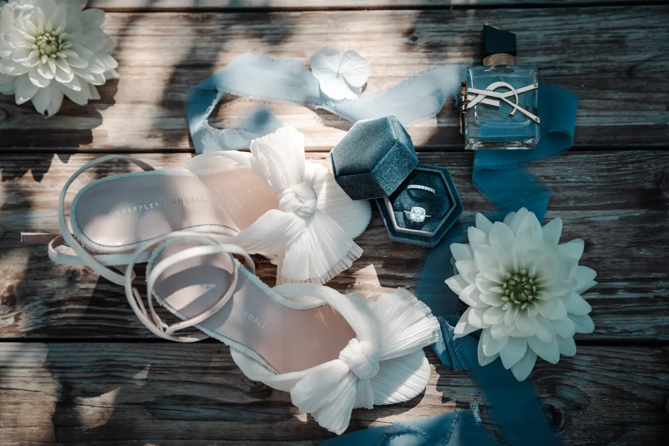 Flatlay mit 2 Brautschuhen, Eheringen, Parfüm und Blumen als Deko