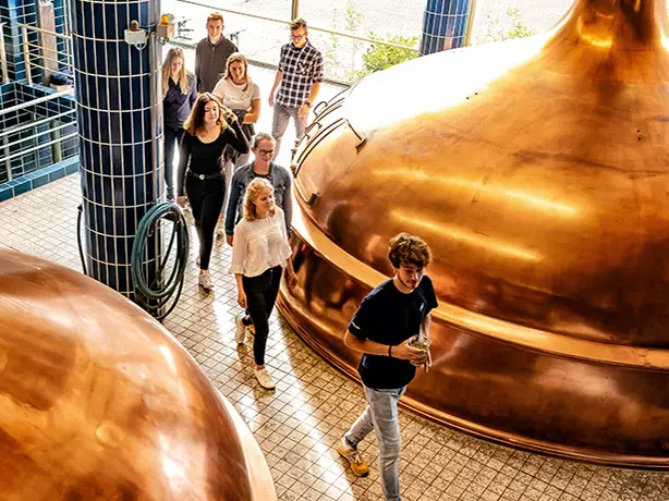Eine Besichtigungsgruppe läuft durch das Sudhaus der Flensburger Brauerei an den Würzekochkesseln aus Kupfer vorbei.