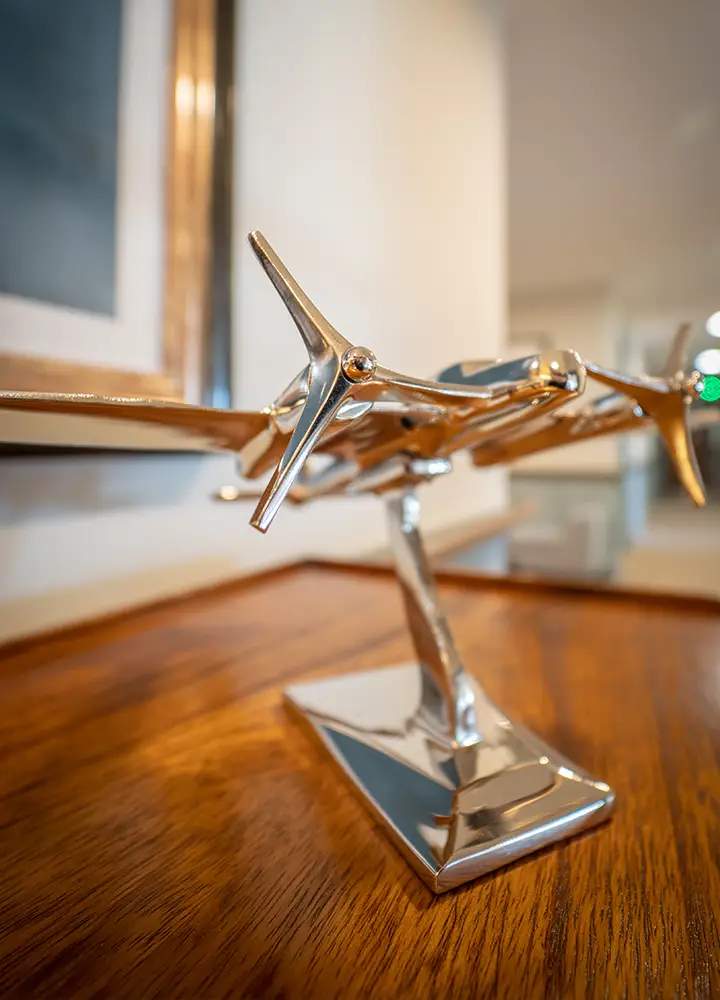 Morar Living Care Home - Hatfield Manor - model aircraft on wooden sideboard. The plane is made out of a silver metal and has two propellers, one on either wing.