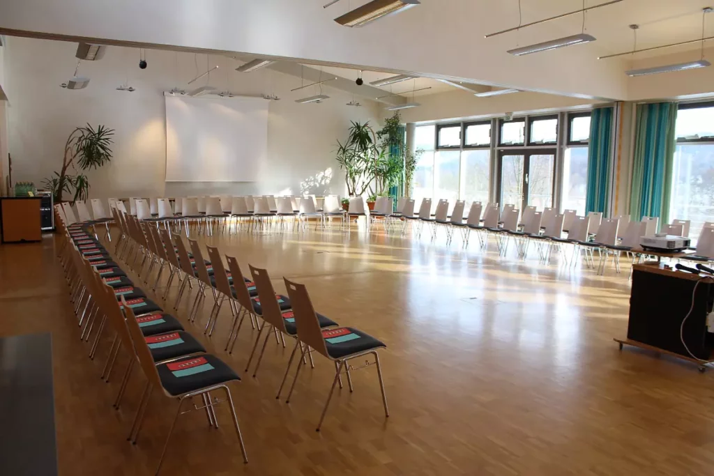 Ein Tagungsraum mit großen Fenstern, in dem zwei Stuhlreihen in U-Form aufgestellt sind