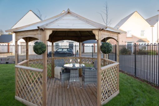 Garden table and chairs under a wooden roof pergola. Blanket on chair and two win glasses on table.