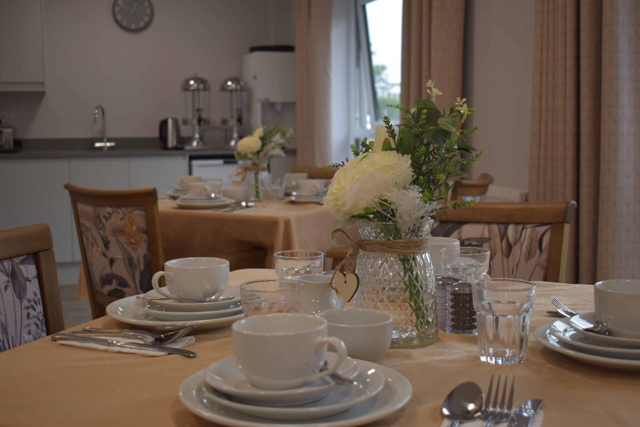 Elegant dining setup with white tableware, floral centerpieces, and soft lighting in a cozy care home dining area.